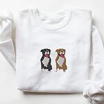 White crewneck sweatshirt laid flat, embroidered with a black and white tuxedo pit bull and a fawn pit bull sitting side by side with their tongues out, centered on the chest