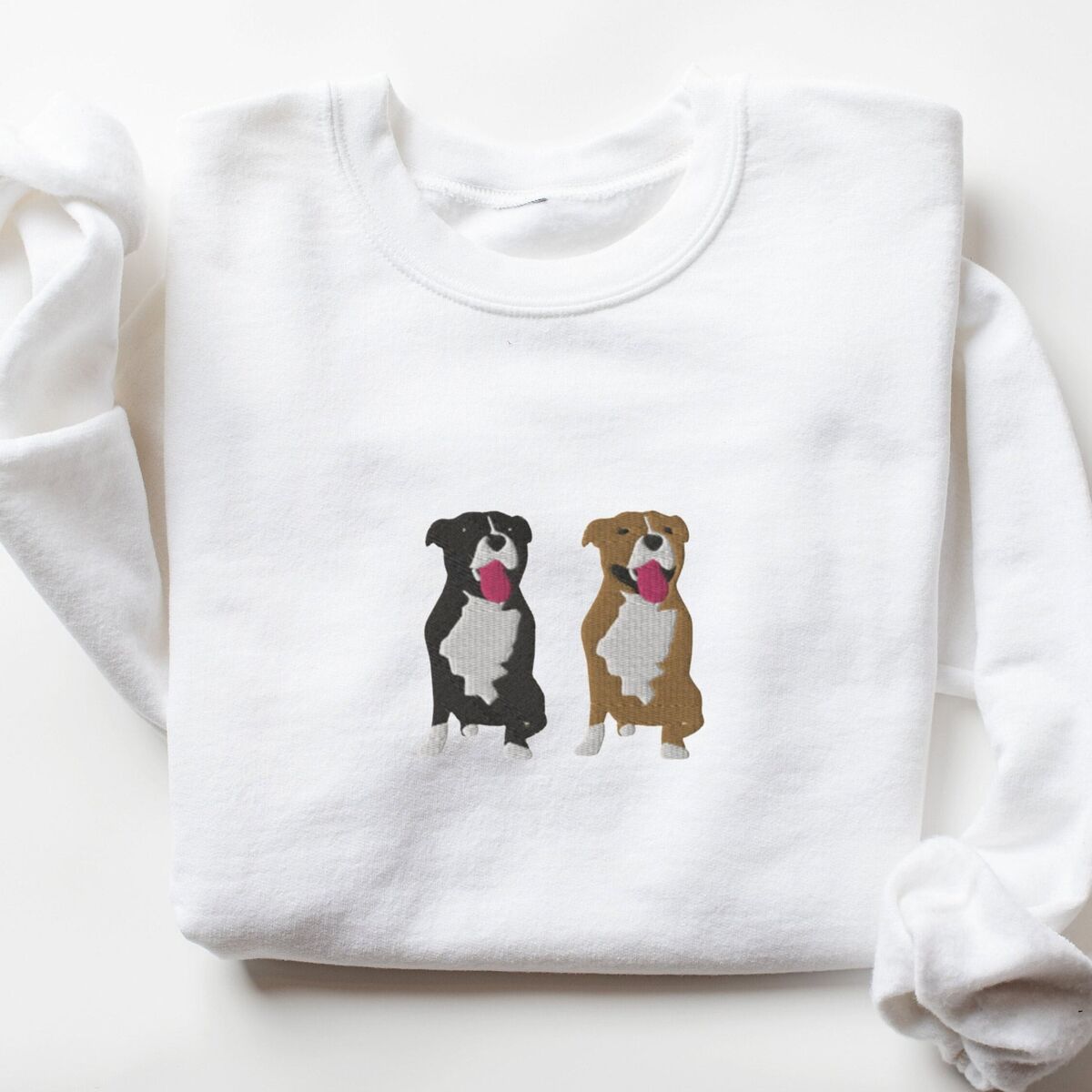 Two Pitbulls Sweatshirt - White White crewneck sweatshirt laid flat, embroidered with a black and white tuxedo pit bull and a fawn pit bull sitting side by side with their tongues out, centered on the chest