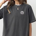 Woman with a gold necklace in a Pepper T-shirt embroidered with a white cartoon doodle face with a black outline and a pink tongue on the left chest