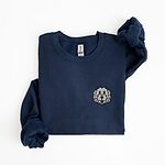 Navy crewneck sweatshirt laid flat on a white background, embroidered with a white cartoon doodle face with a black outline and a pink tongue on the left chest