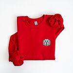 Red crewneck sweatshirt laid flat on a white background, embroidered with a white cartoon doodle face with a black outline and a pink tongue on the left chest