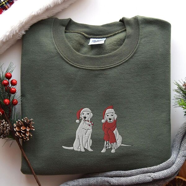 Military Green crewneck sweatshirt laid flat with pine cones and red berries, embroidered with two white labs in Santa hats, one holding a candy cane and one in a long red scarf