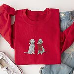 Red crewneck sweatshirt laid flat with jeans and white sneakers, embroidered with two white labs in Santa hats, one holding a candy cane and one in a long red scarf