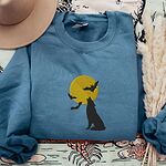 Indigo Blue crewneck sweatshirt folded with a tan felt hat and pampas grass, embroidered with a black wolf silhouette howling at a yellow full moon with three bats