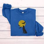 Royal crewneck sweatshirt folded on white wooden boards, embroidered with a black wolf silhouette howling at a yellow full moon with three bats