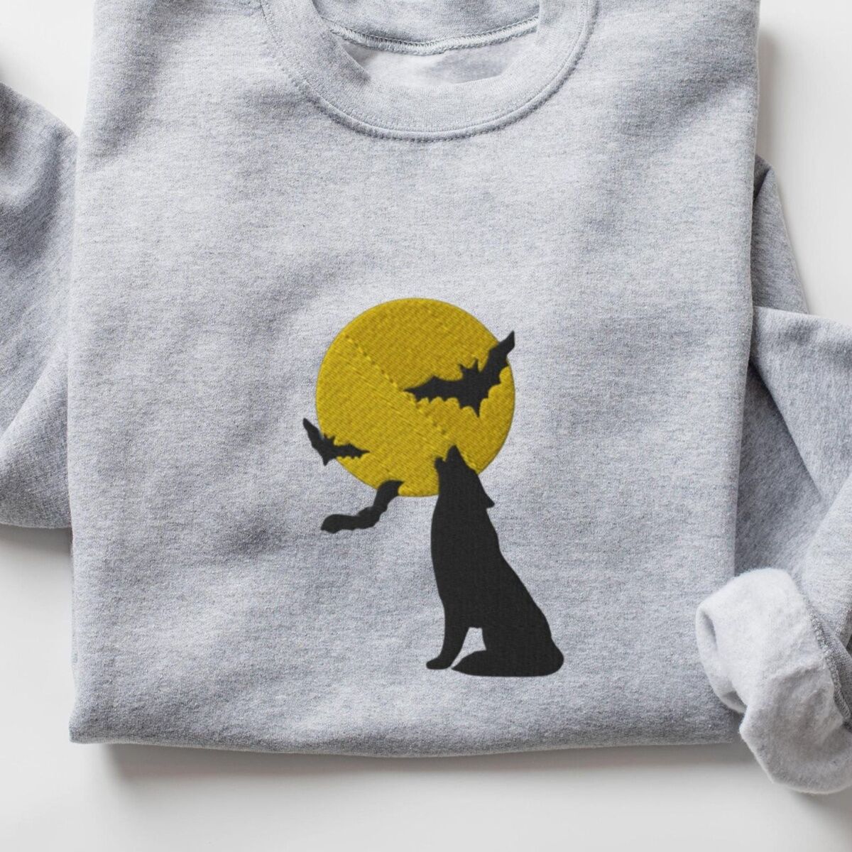 Wolf Howling at the Moon Sweatshirt – Sport Grey Sport Grey crewneck sweatshirt laid flat, embroidered with a black wolf silhouette howling at a yellow full moon with three bats