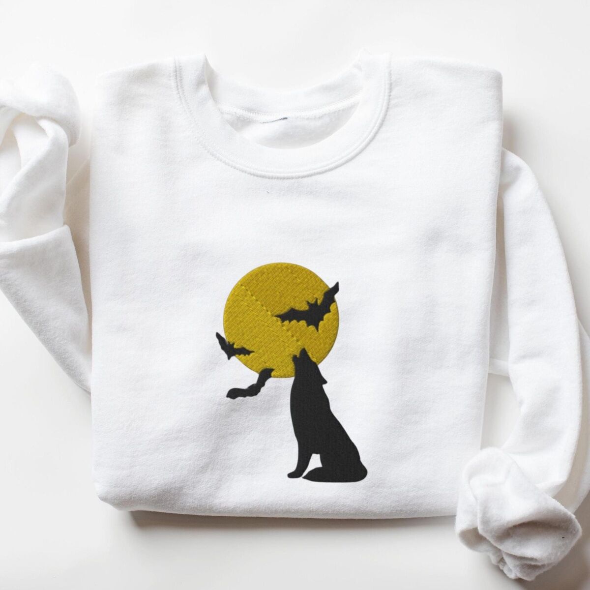 Wolf Howling at the Moon Sweatshirt – White White crewneck sweatshirt laid flat on a white background, embroidered with a black wolf silhouette howling at a yellow full moon with three bats