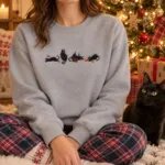 Woman in a Sport Grey holiday cat sweatshirt sitting by a Christmas tree with her black cat