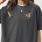 Woman in a Pepper T-shirt with a white tee underneath, a golden lab carrying a flag on the left chest