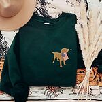Forest Green crewneck sweatshirt beside a hat and dried grass, a yellow lab carrying an American flag stitched on the left chest