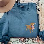 Indigo Blue crewneck sweatshirt beside a hat and dried grass, a golden lab silhouette holding a USA flag on the left chest