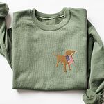 Military Green crewneck sweatshirt laid flat with a rolled sleeve, a golden yellow lab holding a USA flag stitched on the left chest