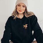 Woman in a beanie wearing a black sweatshirt with a small golden lab and American flag stitched on the left chest