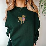 Woman in a dark green crewneck sweatshirt with a golden yellow lab carrying a stars-and-stripes flag centered on the chest