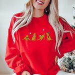 Smiling woman by a Christmas tree in a Red crewneck sweatshirt embroidered with four playful yellow labs in a Santa hat, an elf hat, a red bow and a striped scarf under silver stars