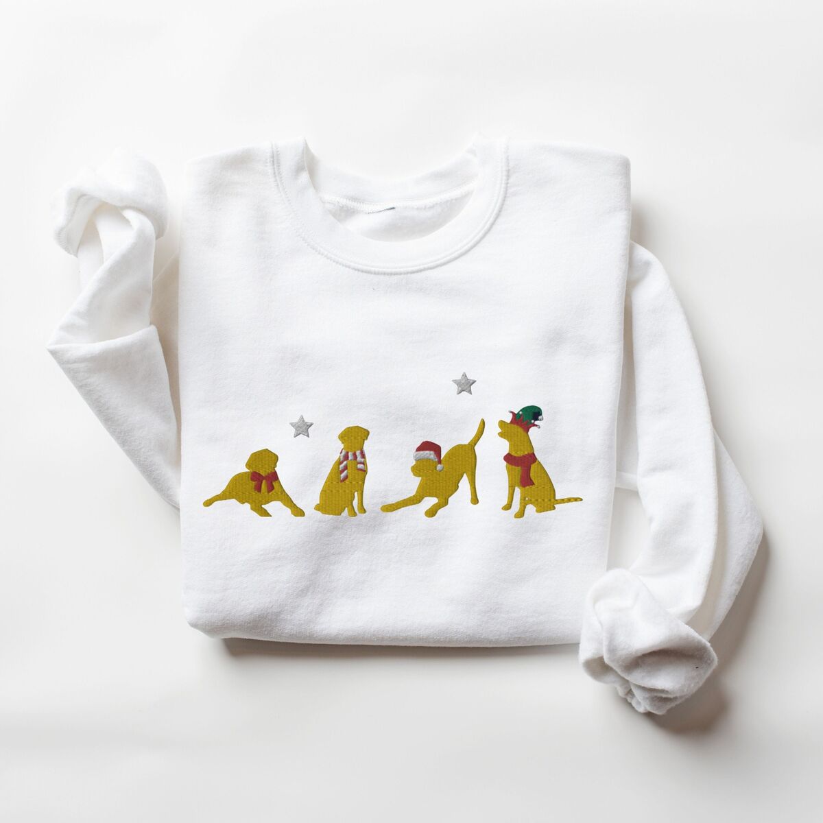Yellow Lab Christmas Sweatshirt - White White crewneck sweatshirt laid flat with folded sleeves, embroidered with four playful yellow labs in a Santa hat, an elf hat, a red bow and a striped scarf under silver stars