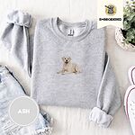 Ash crewneck sweatshirt folded with denim shorts, white sneakers and a potted plant, embroidered with a smiling yellow Labrador lying down with its front paws stretched out