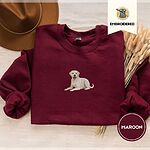 Maroon crewneck sweatshirt with a brown felt hat and dried bunny tail grass, embroidered with a smiling yellow Labrador lying down with its front paws stretched out
