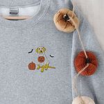Sport Grey crewneck sweatshirt hung beside knitted pumpkins, embroidered with a yellow Labrador in a ghost costume holding a jack-o'-lantern bucket