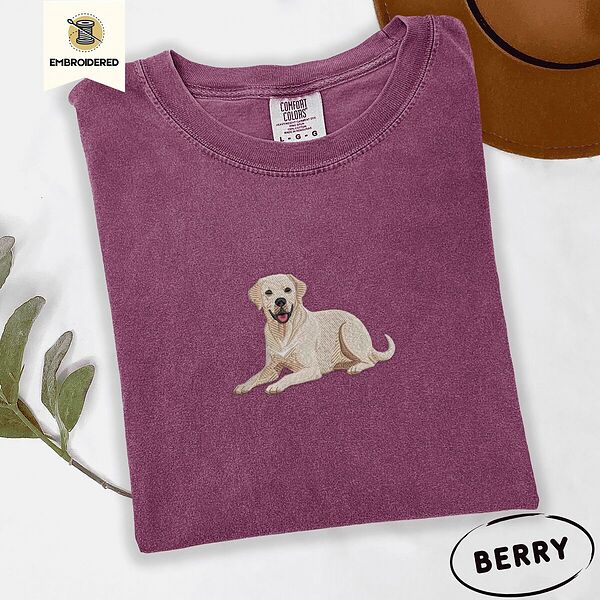 Berry Comfort Colors T-shirt embroidered with a smiling yellow Labrador lying down with its front paws stretched out