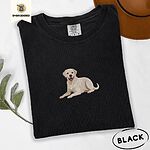 Black Comfort Colors T-shirt embroidered with a smiling yellow Labrador lying down with its front paws stretched out
