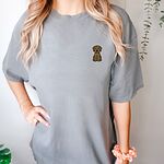 Woman in a Grey T-shirt embroidered with a small golden cartoon Labrador puppy sitting with floppy ears on the left chest