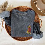 Dark Heather crewneck sweatshirt folded in a wicker basket with a hat, embroidered with a small yellow Labrador in a red Santa hat and a long fringed red scarf on the left chest