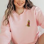 Smiling woman in a Light Pink crewneck sweatshirt embroidered with a small yellow Labrador in a red Santa hat and a long fringed red scarf on the left chest