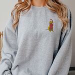 Woman in a Sport Grey crewneck sweatshirt embroidered with a small yellow Labrador in a red Santa hat and a long fringed red scarf on the left chest