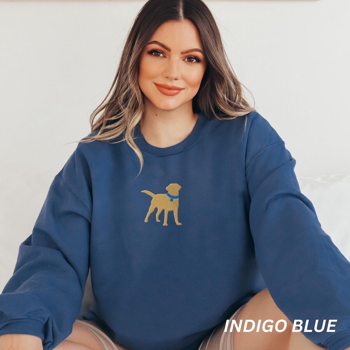 Yellow Lab Silhouette Sweatshirt – Indigo Blue Smiling woman in an Indigo Blue crewneck sweatshirt embroidered with a golden yellow Labrador silhouette standing in a blue collar and round tag in the center of the chest