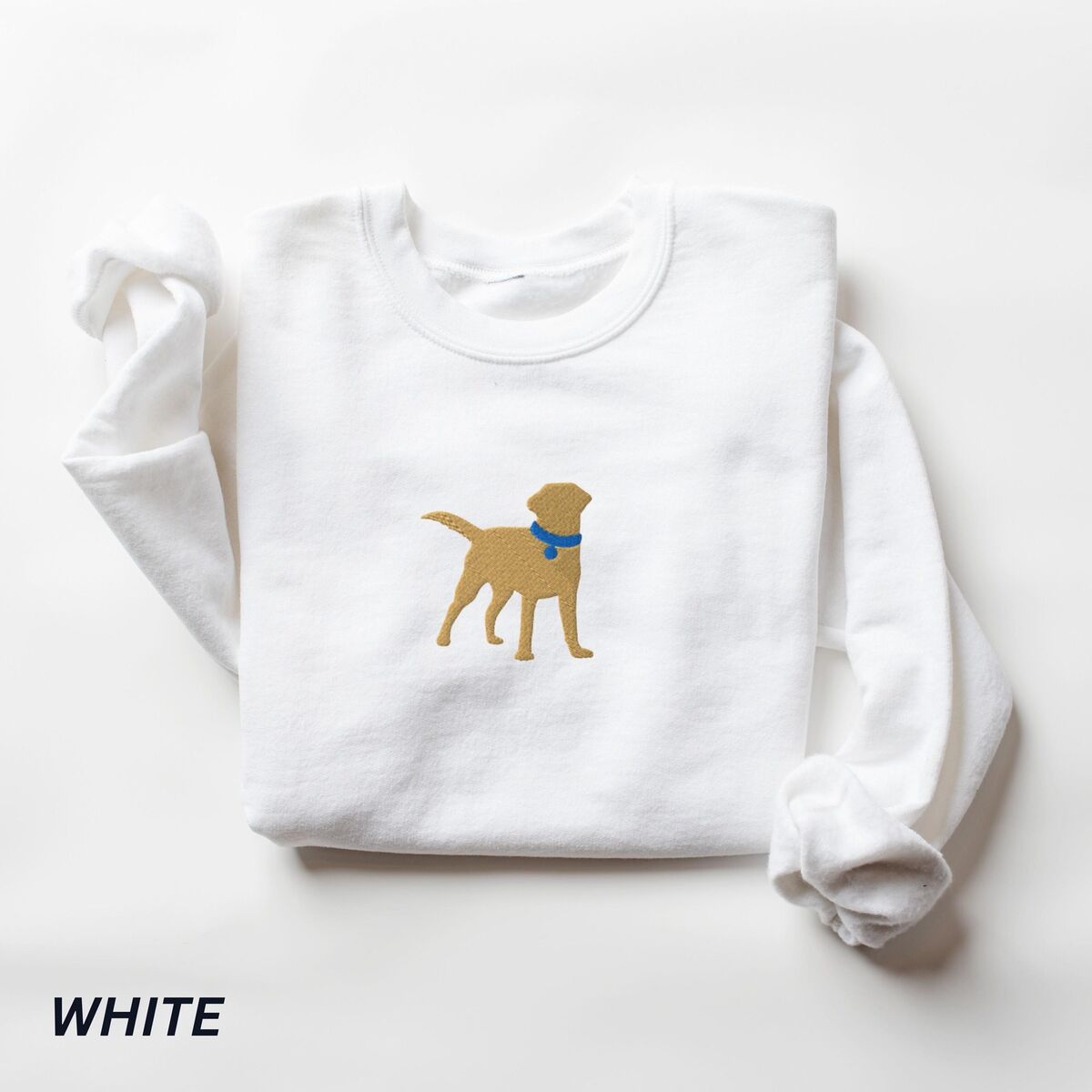 Yellow Lab Silhouette Sweatshirt - White White crewneck sweatshirt laid flat on white, embroidered with a golden yellow Labrador silhouette standing in a blue collar and round tag in the center of the chest