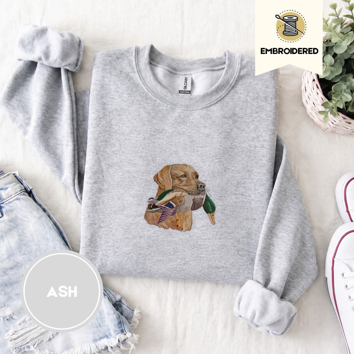 Yellow Lab Sweatshirt – Ash Ash crewneck sweatshirt folded with denim shorts, white sneakers and a potted plant, embroidered with a yellow Labrador head carrying a mallard drake in its mouth