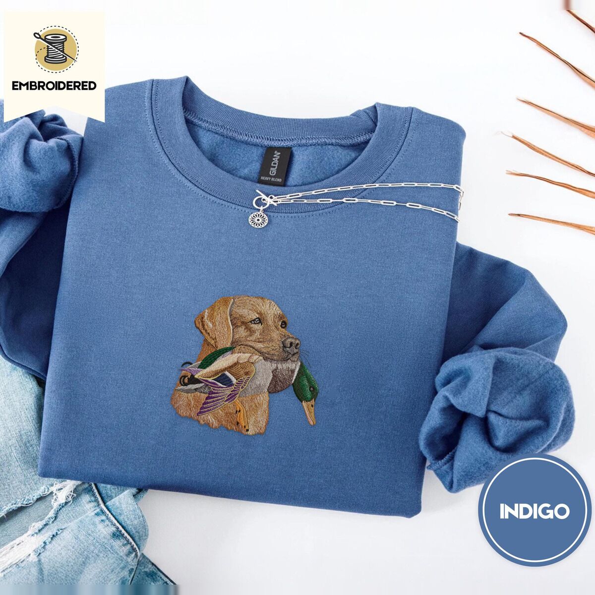 Yellow Lab Sweatshirt – Indigo Blue Indigo Blue crewneck sweatshirt folded with light jeans and dried twigs, embroidered with a yellow Labrador head carrying a mallard drake in its mouth
