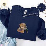Navy crewneck sweatshirt folded with ripped jeans and a silver chain necklace, embroidered with a yellow Labrador head carrying a mallard drake in its mouth