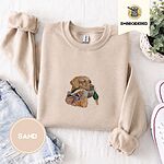 Sand crewneck sweatshirt folded with denim shorts, white sneakers and a potted plant, embroidered with a yellow Labrador head carrying a mallard drake in its mouth